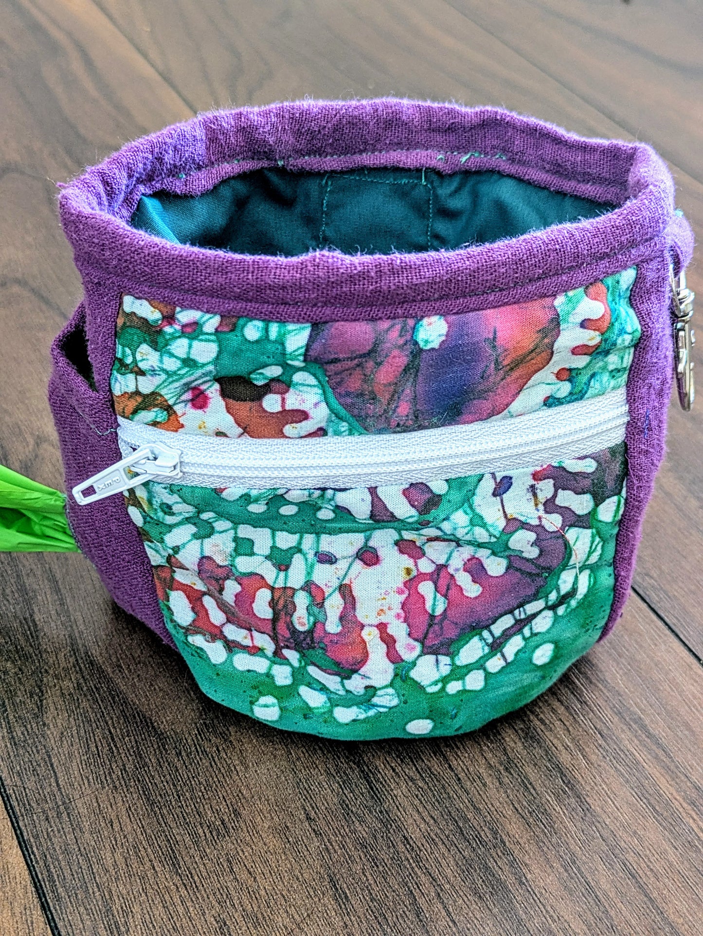 Purple and green dog treat pouch made from upcycled fabric. Has wipeable lining, zip front pocket, poo bag holder, clip for keys and a belt loop attachment for hands free training.
